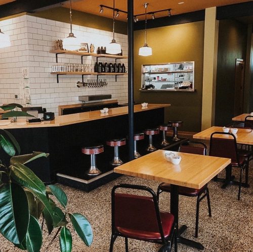 A cozy café interior featuring a bar with stools, wooden tables, and green walls, creating a warm atmosphere.