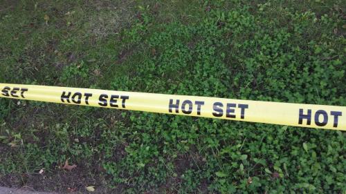 Yellow caution tape reading "HOT SET" laid across green grass.