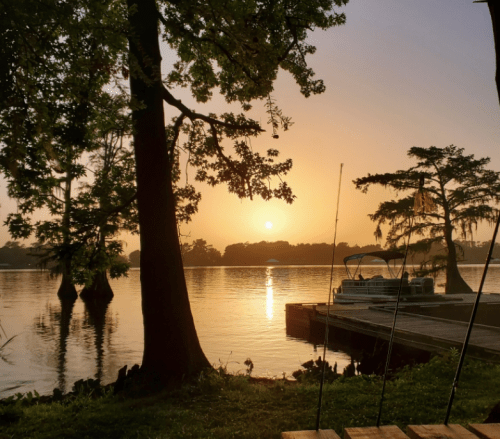 Sunrise over a calm lake, with trees and a dock in the foreground, creating a serene and peaceful atmosphere.