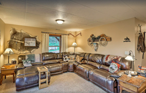 Cozy living room with a large leather sectional, rustic decor, and a window overlooking greenery.