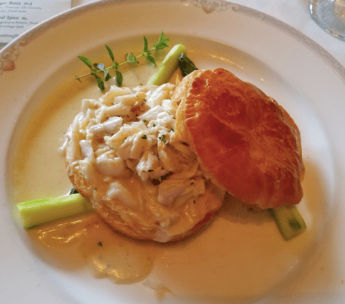 A flaky biscuit topped with crab meat and creamy sauce, garnished with fresh herbs and served on a plate.