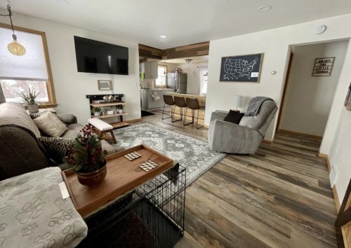 Cozy living room with a sofa, TV, and dining area, featuring a rug, plants, and a pet crate in a bright, inviting space.