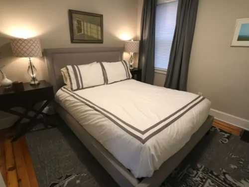 Cozy bedroom featuring a queen bed with gray accents, two lamps, and a decorative rug.