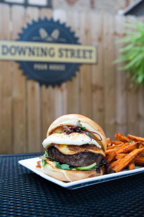 A gourmet burger topped with a fried egg, served with sweet potato fries, against a rustic outdoor backdrop.