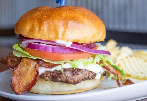 A juicy burger with bacon, lettuce, tomato, onion, and mayo on a toasted bun, served with wavy potato chips.