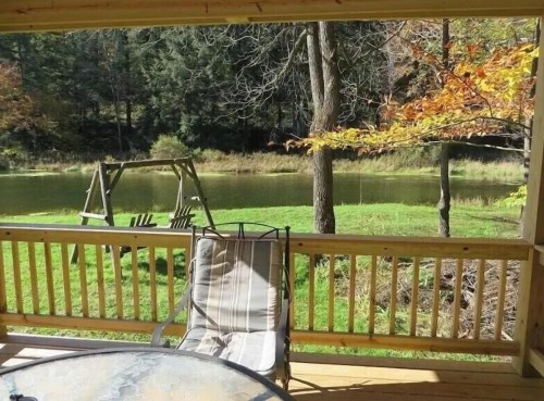 A peaceful view from a porch overlooking a pond, with a swing set and autumn foliage in the background.
