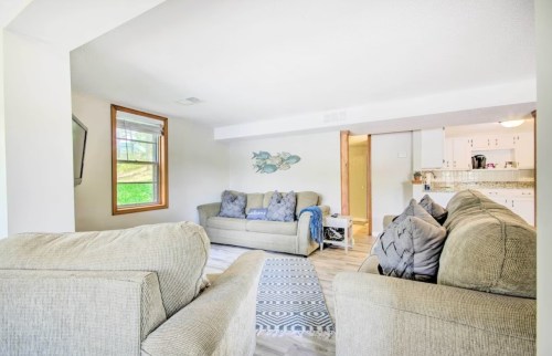 Bright living room with two sofas, decorative fish artwork, and a view into a kitchen area. Light wood flooring.
