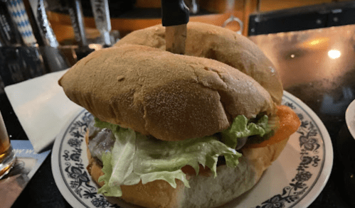 A large sandwich with lettuce, tomato, and a knife inserted, served on a decorative plate.