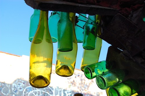 Colorful glass bottles in yellow and green hanging from a structure against a blue sky.