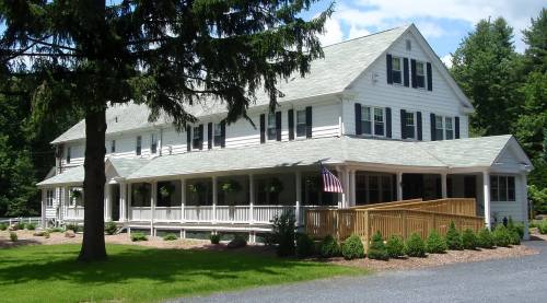 A large white house with green shutters and a porch, surrounded by trees and a well-maintained lawn. An American flag is displayed.