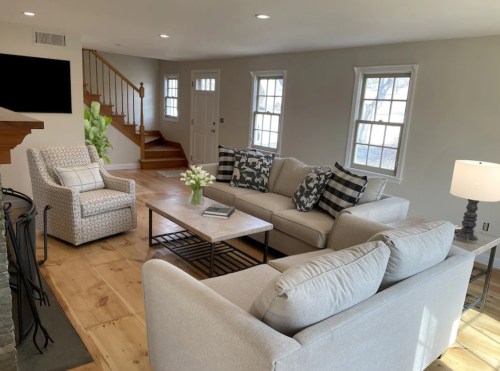 Cozy living room with two sofas, a coffee table, and a chair, featuring light colors and natural light from windows.