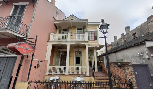 A colorful two-story house with a porch, surrounded by brick walls and outdoor seating, in a historic neighborhood.