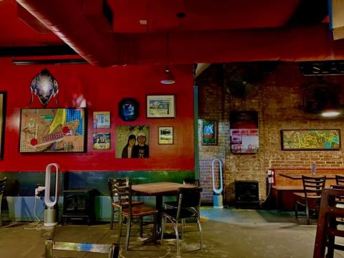 Cozy restaurant interior with red walls, artwork, wooden tables, and a mix of modern and rustic decor.
