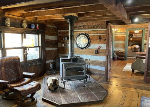 Cozy interior of a rustic cabin featuring a wood stove, leather chair, and wooden beams. Warm and inviting atmosphere.