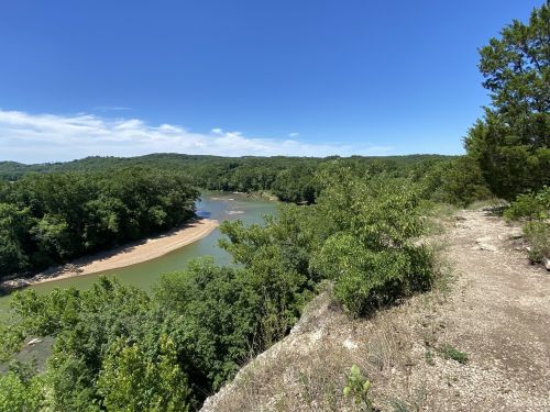 A scenic view of a river winding through lush green trees under a clear blue sky.