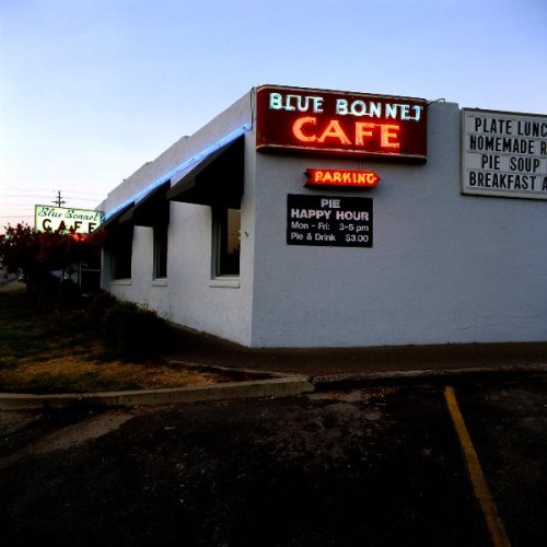 A corner view of the Blue Bonnet Cafe with neon signs for parking and happy hour specials.