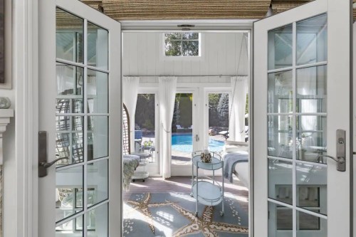 A view through double doors into a bright, airy room with a pool visible outside.