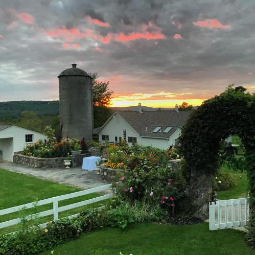 A picturesque farm scene at sunset, featuring a silo, blooming flowers, and a vibrant sky with clouds.