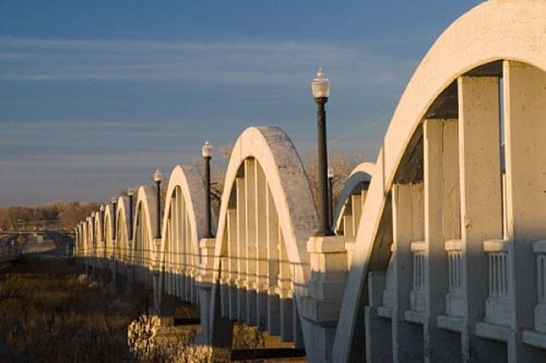 A series of arched concrete bridge spans under a clear sky, with street lamps lining the structure.