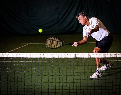 A man in a white shirt hits a tennis ball with a racket on an indoor court, focused on the game.