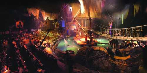 A vibrant pirate-themed stage with a ship, water, and an audience, set in a dimly lit arena.