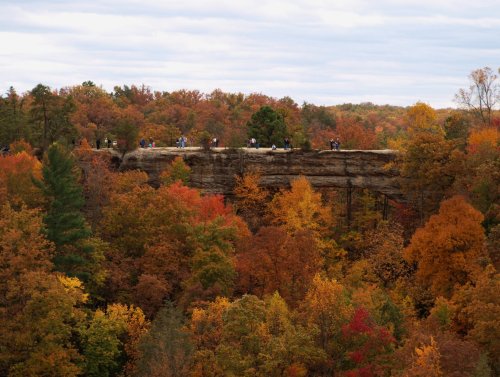A scenic view of a rocky outcrop surrounded by vibrant autumn foliage and people enjoying the landscape.