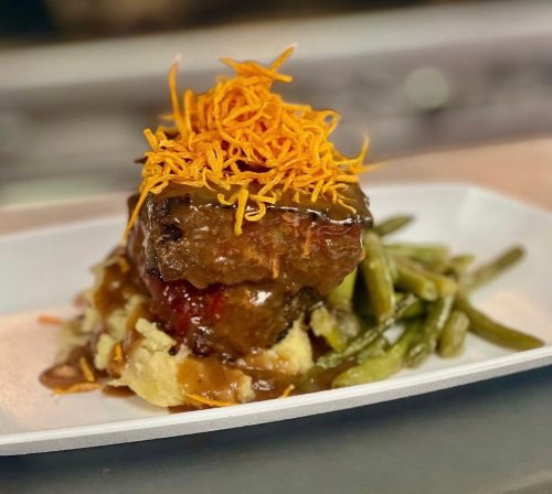 A plated meal featuring meatloaf topped with shredded cheese, served with mashed potatoes and green beans.