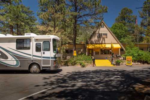 An RV parked in front of a yellow-roofed lodge surrounded by trees on a sunny day.