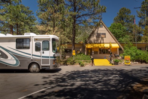 An RV parked in front of a yellow-roofed lodge surrounded by trees on a sunny day.