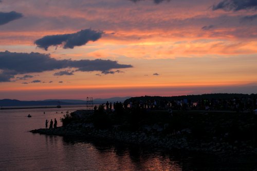 Silhouetted figures by a lake at sunset, with vibrant orange and purple skies reflecting on the water.