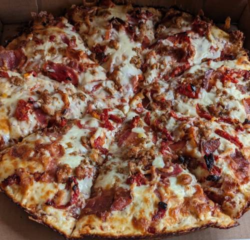 A close-up of a pizza topped with cheese, pepperoni, sausage, and crispy bacon in a pizza box.