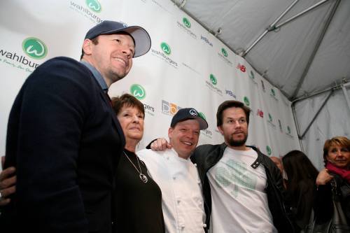 A group of four people, including two men in caps and a woman, pose together at a Wahlburgers event.