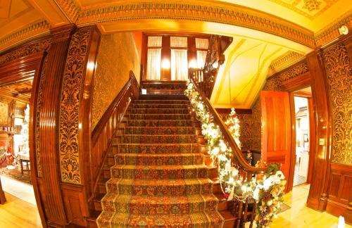 A grand staircase with ornate woodwork and patterned carpet, decorated with festive garlands and lights.