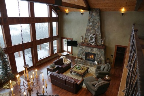 Cozy living room with a stone fireplace, large windows, and rustic decor, overlooking a snowy landscape.