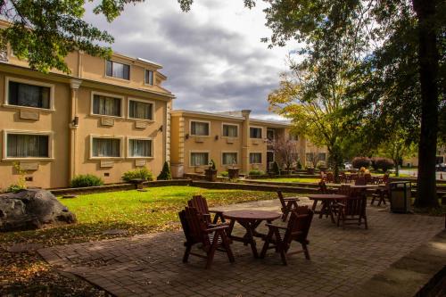 A peaceful courtyard with wooden tables and chairs, surrounded by trees and a two-story building under a cloudy sky.