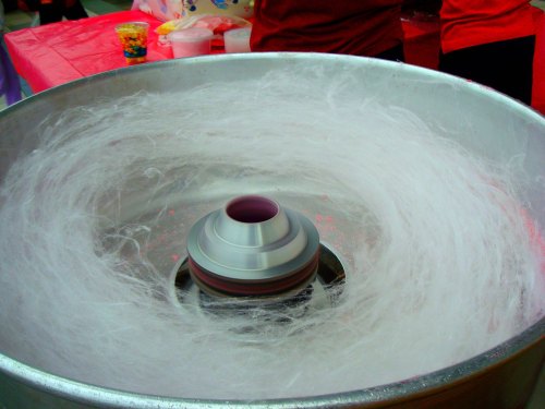 A cotton candy machine with fluffy, spun sugar swirling inside a metal bowl.