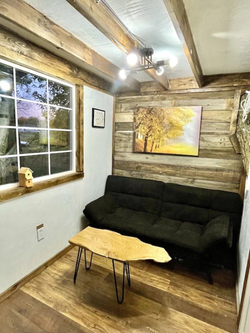 Cozy room with a black sofa, wooden coffee table, and a nature-themed wall art, featuring a window and rustic decor.