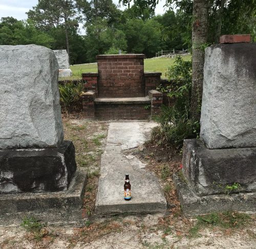 A path between two large stone pillars leads to a brick structure, with a bottle placed in the center.