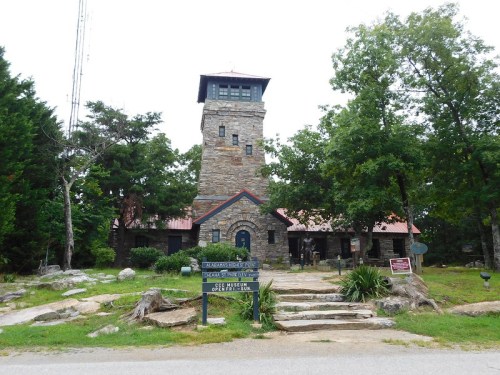 Stone building with a tower, surrounded by trees, featuring a sign for a museum and steps leading to the entrance.