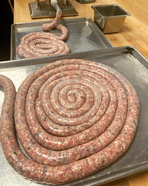 Coiled sausage links on a metal tray, showcasing a spiral shape and raw meat texture.