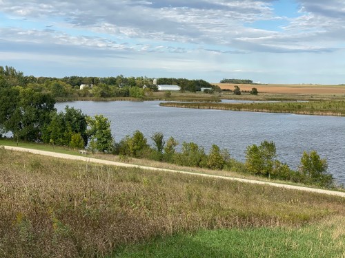 A serene landscape featuring a winding river, lush greenery, and distant farmland under a partly cloudy sky.