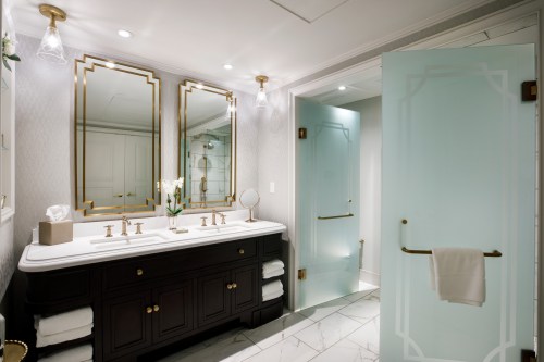 Luxurious bathroom featuring dual mirrors, elegant fixtures, and a frosted glass door. Soft lighting enhances the decor.