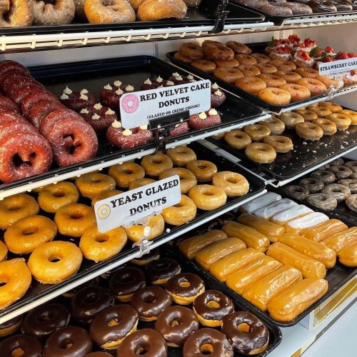 A display case filled with various donuts, including red velvet, glazed, and strawberry cake donuts.