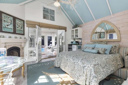 Cozy bedroom with a patterned bedspread, large windows, and a charming decor featuring light blue and natural wood tones.