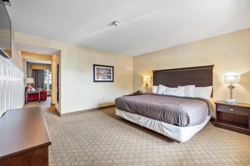 A spacious hotel room featuring a king-sized bed, nightstands, a dresser, and a view of a hallway.