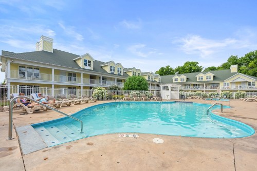 A clear blue pool surrounded by lounge chairs and a yellow building with balconies under a blue sky.