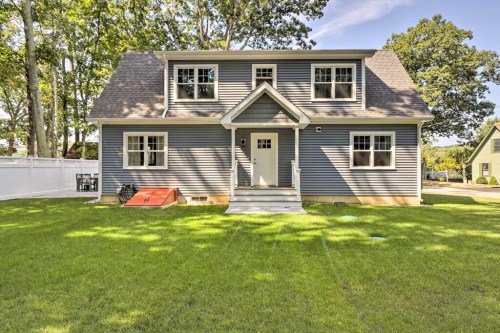 A modern two-story house with gray siding, white trim, and a front lawn surrounded by trees.