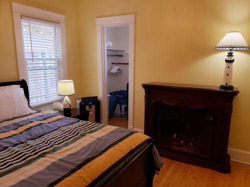 Cozy bedroom with a bed, lamp, fireplace, and a closet in a yellow-walled room.