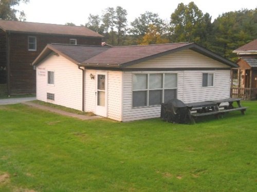 A single-story house with a sloped roof, large windows, and a picnic table in the grassy yard. Trees are in the background.