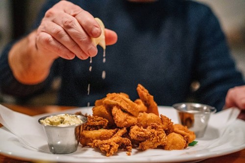 A hand squeezes lemon over a plate of fried seafood, accompanied by dipping sauces.